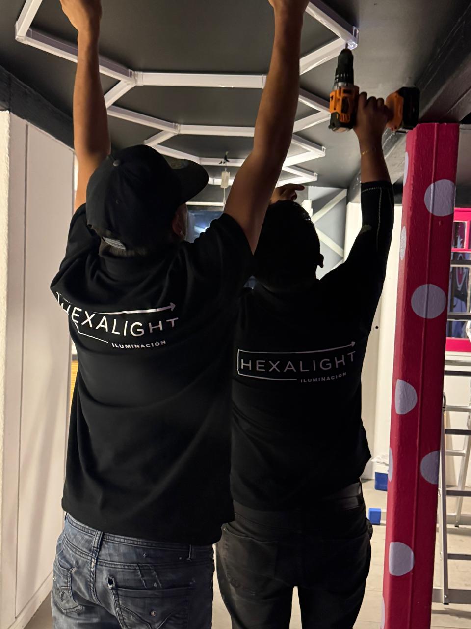 Dos técnicos HexaLight fijando soportes con taladro para hexágonos LED en techo