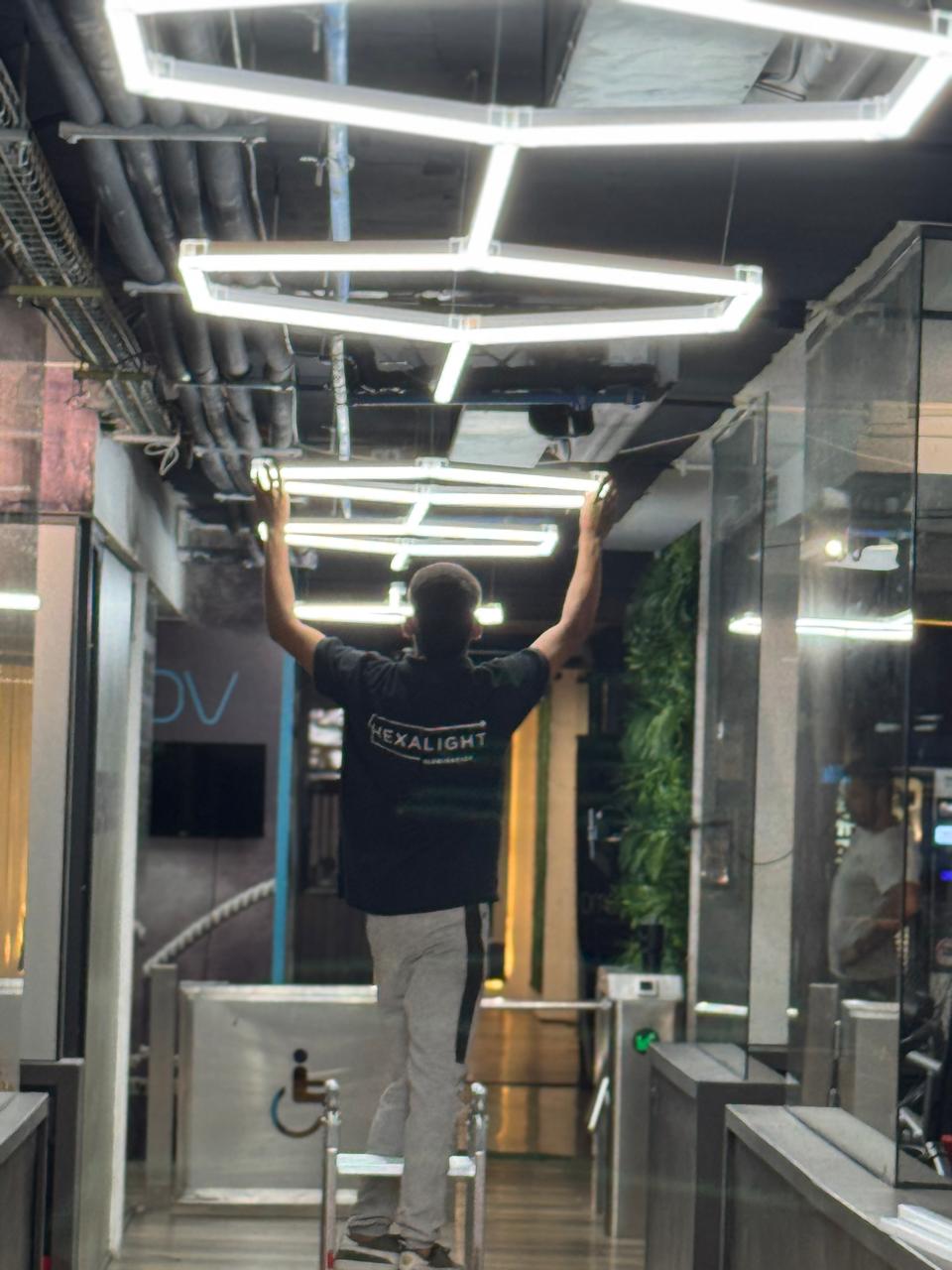 Técnico HexaLight montando panel hexagonal LED en techo de local comercial