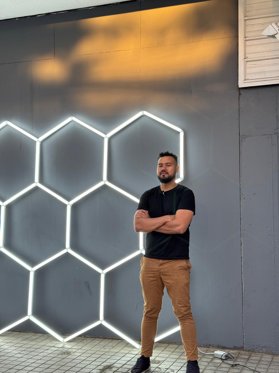Jhonathan Blanco, fundador de HexaLight, frente a instalación de hexágonos LED en pared